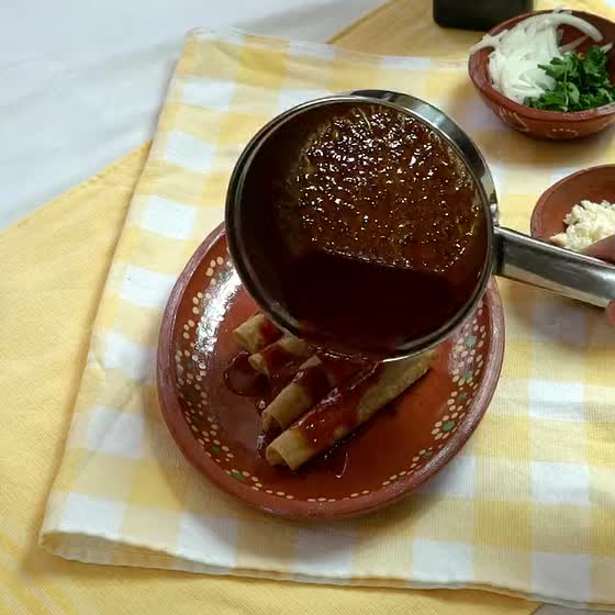 Mole coloradito poured over crispy chicken taquitos
