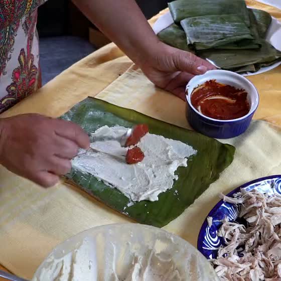 Mole rojo spooned onto the masa of a banana leaf tamal